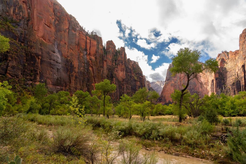 Red rock cliffs tower over a green valley and river.